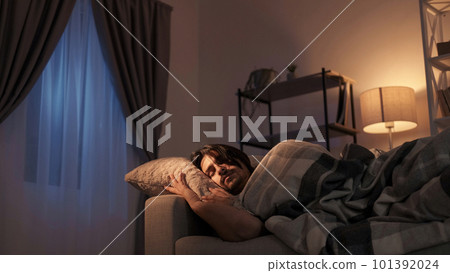Night rest. Home relaxation. Cozy evening. Tired peaceful man sleeping on soft pillow under blanket on couch at dark living room interior. 101392024