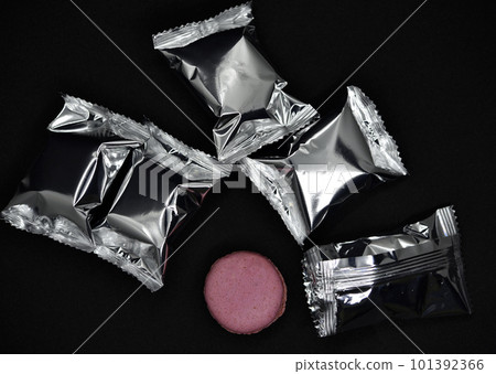 Macaroons on a shiny wrapper. Colorful delicious macaroons on a black background. Shiny cookie wrapper. 101392366