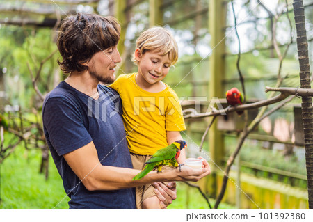 Dad and son feed the parrot in the park. Spending time with kids concept Dad and son feed the parrot in the park. Spending time with kids concept 101392380