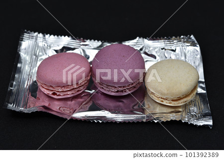 Macaroons on a shiny wrapper. Colorful delicious macaroons on a black background. Shiny cookie wrapper. 101392389