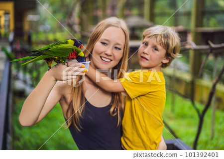 Mom and son feed the parrot in the park. Spending time with kids concept Mom and son feed the parrot in the park. Spending time with kids concept 101392401