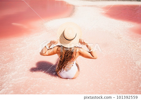 A woman traveler looks at an amazing pink salt lake. He sits with his back in a bathing suit and holds his hat in his hands. Wanderlust travel concept 101392559