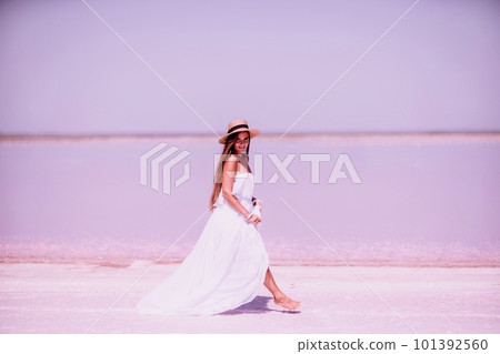 Woman in pink salt lake. She walks in a white long dress and hat along the salty white shore of the lake. Wanderlust photo for memory 101392560