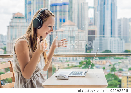 Young woman teaches a foreign language or learns a foreign language on the Internet on her balcony against the backdrop of a big city. Online language school lifestyle Young woman teaches a foreign language or learns a foreign language on the Internet on her balcony against the backdrop of a big city. Online language school lifestyle 101392856
