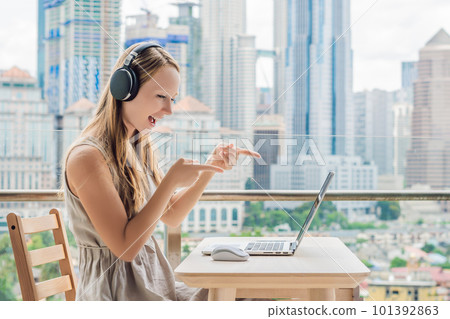 Young woman teaches a foreign language or learns a foreign language on the Internet on her balcony against the backdrop of a big city. Online language school lifestyle 101392863