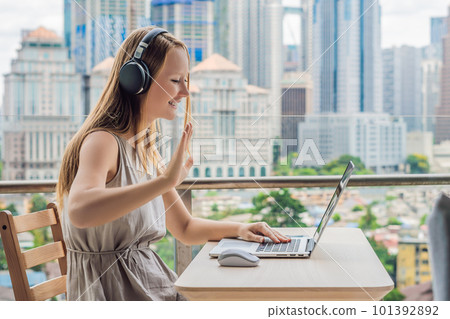 Young woman teaches a foreign language or learns a foreign language on the Internet on her balcony against the backdrop of a big city. Online language school lifestyle 101392892