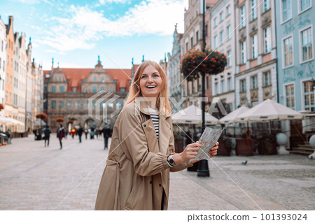 Happy young woman tourist with trendy look with map visiting city and looking around, searching direction on location map during vacation in Gdansk old town. Happy young woman tourist with trendy look with map visiting city and looking around, searching direction on location map during vacation in Gdansk old town. 101393024