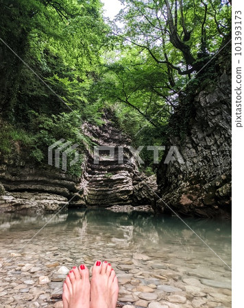 Female red pedicure feet refreshing in the river clear water of mountain stream, on the background cliff Female red pedicure feet refreshing in the river clear water of mountain stream, on the background cliff 101393173