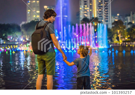 Dad and son tourists on background of colorful fountain on the lake at night, near by Twin Towers with city on background. Kuala Lumpur, Malaysia 101393257