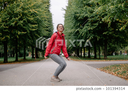Young caucasian woman girl with toothy smile jumping in park forest outdoors looking at camera. 101394314