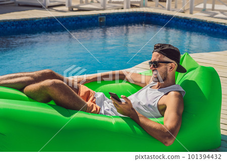 Young man enjoying leisure, lying on the air sofa Lamzac, near the pool Young man enjoying leisure, lying on the air sofa Lamzac, near the pool 101394432