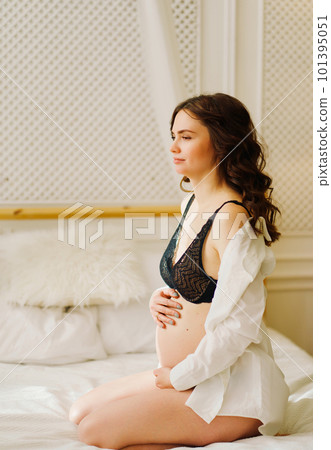 a slender pregnant woman in a black underwea and white shirt on the bed a slender pregnant woman in a black underwea and white shirt on the bed 101395051