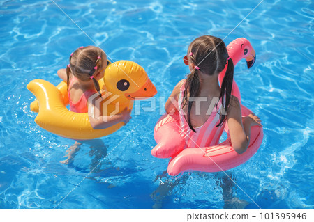 Two girls with circles in the shape of flamingos and ducks swim in the clear clear water of the sea. Two girls with circles in the shape of flamingos and ducks swim in the clear clear water of the sea. 101395946