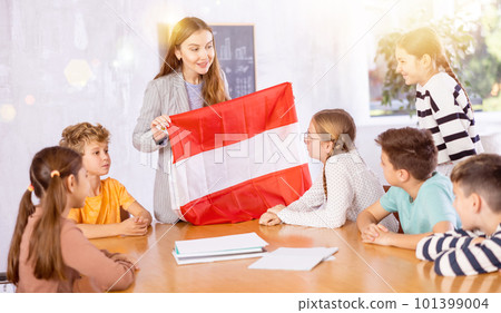 Young woman teacher demonstrating flag of Austria for schoolkids preteens during lesson of geography in classroom Young woman teacher demonstrating flag of Austria for schoolkids preteens during lesson of geography in classroom 101399004