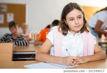 Interested diligent preteen schoolgirl writing exercises at lessons 101399017