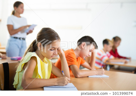 Interested diligent preteen schoolgirl writing exercises at lessons Interested diligent preteen schoolgirl writing exercises at lessons 101399074