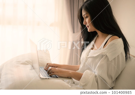 Young woman working on a laptop sitting on bed at home Young woman working on a laptop sitting on bed at home 101400985