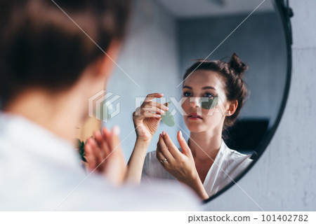 Anti-aging care. A young woman at home in front of the mirror applies patches under her eyes. Anti-aging care. A young woman at home in front of the mirror applies patches under her eyes. 101402782