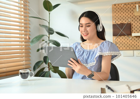 Attractive woman wearing wireless headphone and checking social media or working online on digital tablet 101405646
