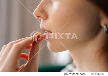Close-up cropped shot of unrecognizable ill young woman taking pill. Closeup side view of depressed redhead female holding antidepressants tablet at mouth. Concept of insurance and healthcare Close-up cropped shot of unrecognizable ill young woman taking pill. Closeup side view of depressed redhead female holding antidepressants tablet at mouth. Concept of insurance and healthcare 101406483