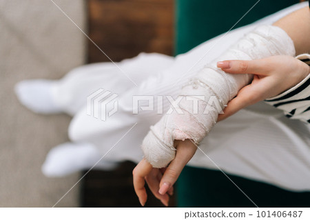 Top view cropped shot of unrecognizable young woman with broken right hand wrapped in white gypsum bandage, gently massaging injured arm. Unhappy female with broken arm from accident at home. Top view cropped shot of unrecognizable young woman with broken right hand wrapped in white gypsum bandage, gently massaging injured arm. Unhappy female with broken arm from accident at home. 101406487