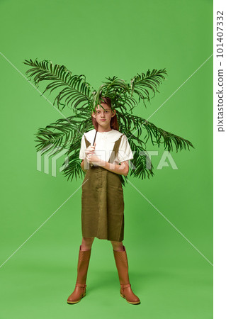 Little pretty girl wearing boots standing with palm instead of umbrella over green background. Tropical rain 101407332