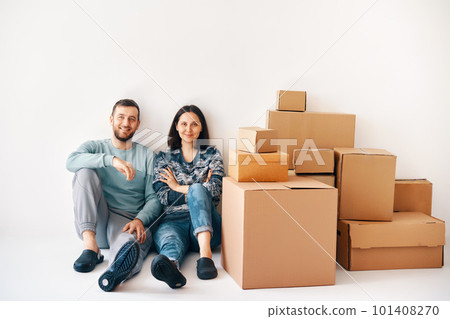Smiling happy couple sitting on floor after the moving to new house with cardboard boxes 101408270