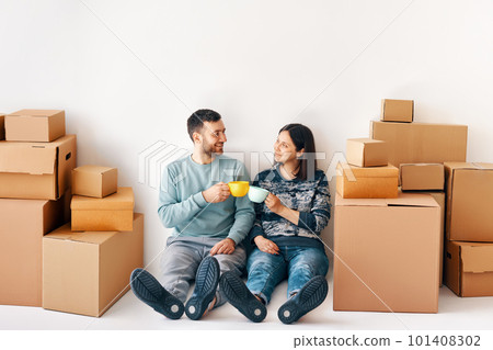 Young couple taking a break on moving day sitting on floor and celebrating their new life with drink 101408302