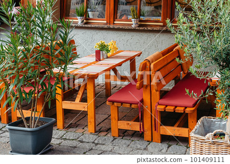 Street terrace of the coffee shop. Wooden tables next to the coffee shop behind green bushes. Coffee shop in the city center. Summer outdoor cafe with stone gray pavement green bushes in tubs sunny Street terrace of the coffee shop. Wooden tables next to the coffee shop behind green bushes. Coffee shop in the city center. Summer outdoor cafe with stone gray pavement green bushes in tubs sunny 101409111