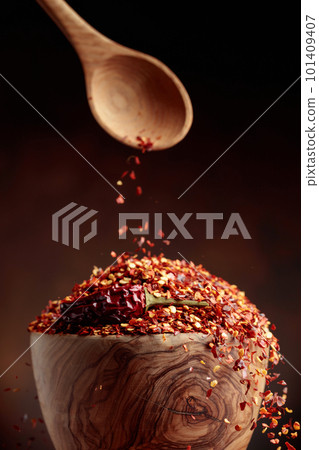 Chilli flakes are poured into a wooden dish. 101409407