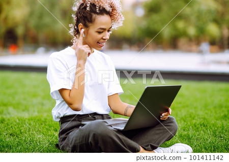 Girl speak talk on video call with colleagues on online briefing on modern laptop sitting in the park.Young woman - freelancer. Girl speak talk on video call with colleagues on online briefing on modern laptop sitting in the park.Young woman - freelancer. 101411142