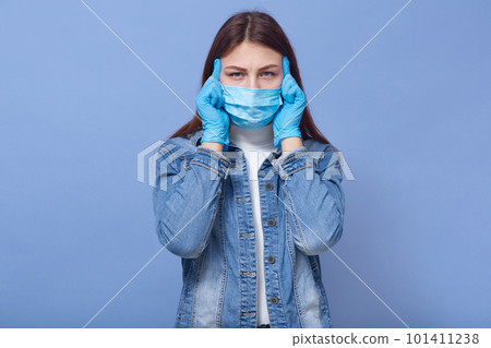 Studio portrait of infected ill young woman putting hands on temple, having headache, feeling unwell, being in self isolation, wearing gloves and protective mask. Coronavirus outbreak concept. Studio portrait of infected ill young woman putting hands on temple, having headache, feeling unwell, being in self isolation, wearing gloves and protective mask. Coronavirus outbreak concept. 101411238
