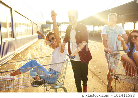 Group of happy young people having fun on shopping trolleys. Multiethnic young people racing on shopping cart. 101411588