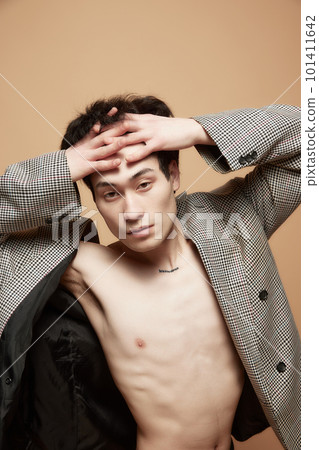 Portrait of young asian man posing shirtless in stylish grey jacket against light brown studio background Portrait of young asian man posing shirtless in stylish grey jacket against light brown studio background 101411642