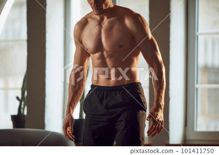 Cropped image of muscular, relief, strong, beautiful body. Male model posing shirtless, training at home on daytime. 101411750