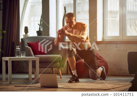 Athletic, sportive young man with muscular strong body, training shirtless at home, doing lunges exercises. Strong relief legs 101411751