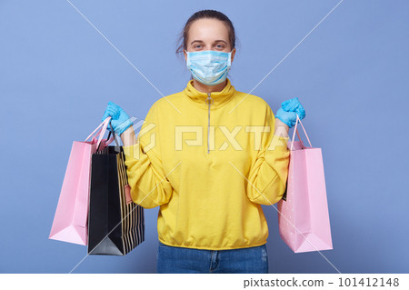 Corona viris, covid 19, health, safety and pandemic concept. Young Caucasian woman wearing protective medical mask, medical gloves for protection from virus disease with shopping bags in hands. 101412148