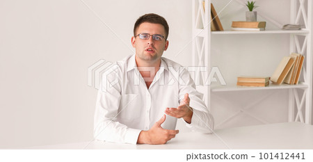 Interview meeting. Male speaker. Office presentation. Smart elegant man in white shirt sitting desk and talking in light room interior. Interview meeting. Male speaker. Office presentation. Smart elegant man in white shirt sitting desk and talking in light room interior. 101412441
