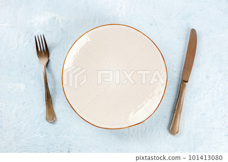 An empty white plate with a gold rim, with a fork and a knife, overhead 101413080