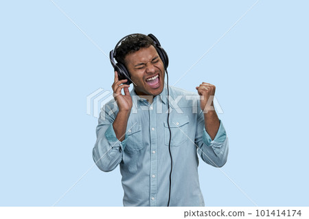Portrait of excited emotional Indian man listen to music in headphones. Isolated on pastel blue background. 101414174
