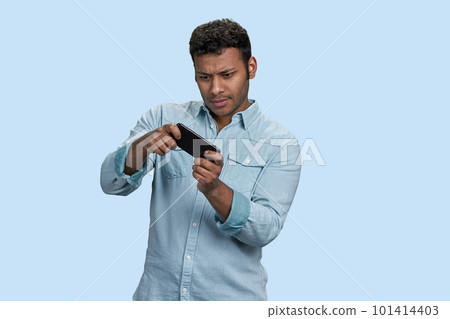 Excited young south asian man playing game in mobile videogame. Isolated on pastel blue background. Excited young south asian man playing game in mobile videogame. Isolated on pastel blue background. 101414403