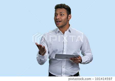 Speech of a young southeast indian man with tablet pc. Isolated on pastel blue background. 101414597