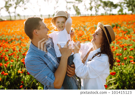 Family with a child walking on a poppy field. Mother, father, little daughter having fun on the poppy field. 101415123