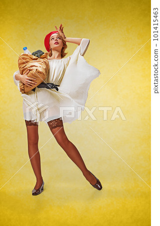 Grocery shopping. Full-length portrait of pretty, young girl in stylish clothes posing with shopping bag over yellow studio background. Pin-up style 101415463