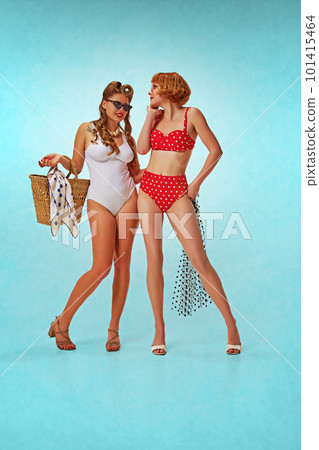 Full-length image of two pretty, beautiful girls in stylish, vintage bodysuits posing against blue studio background. Pin-up style 101415464