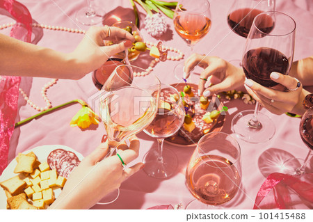 Holidays meeting. Female hands with glassed with red and rose wine on pink textured background, tablecloth with appetizers, snacks 101415488
