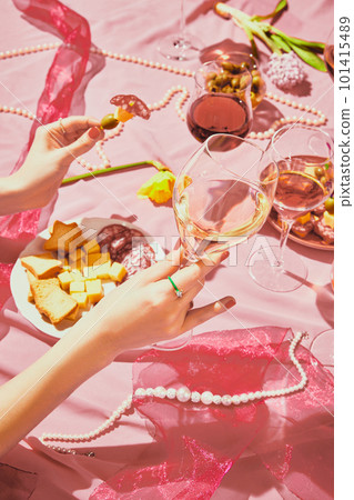 Vertical image of female hand holding glass filled with rose wine on pink textured background, tablecloth with appetizers Vertical image of female hand holding glass filled with rose wine on pink textured background, tablecloth with appetizers 101415489