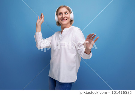 mature woman with blond hairstyle dancing to music in wireless headphones mature woman with blond hairstyle dancing to music in wireless headphones 101416585