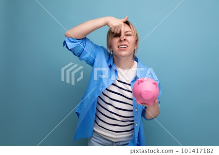 blond neat smiling girl with a grimace holds a piggy bank on a blue background blond neat smiling girl with a grimace holds a piggy bank on a blue background 101417182