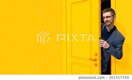 Cheerful, smiling, stylish man in formal wear, businessman peeking out yellow door with coffee. Job fair, employment, education Cheerful, smiling, stylish man in formal wear, businessman peeking out yellow door with coffee. Job fair, employment, education 101417359